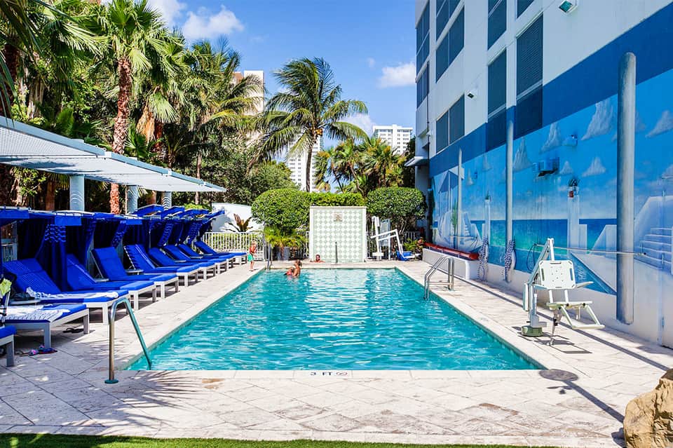 Urban pool deck with bright blue loungers, palm trees, and glass-walled high-rise building