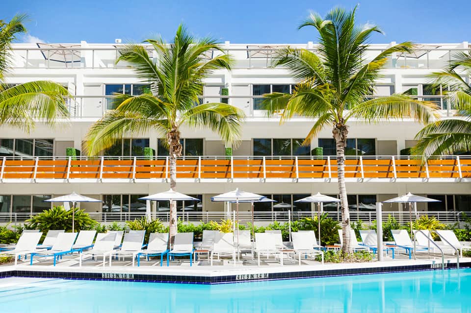 Modern beachfront hotel exterior with white balconies, orange accents, and palm trees
