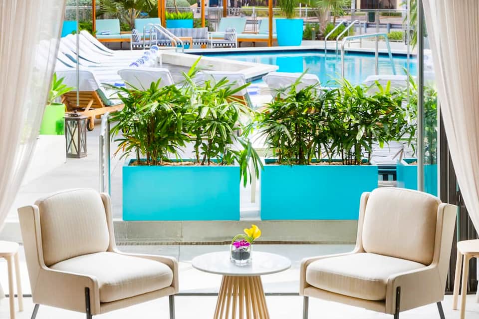 Modern lounge seating with view through glass doors to pool with bright blue planters and palm trees