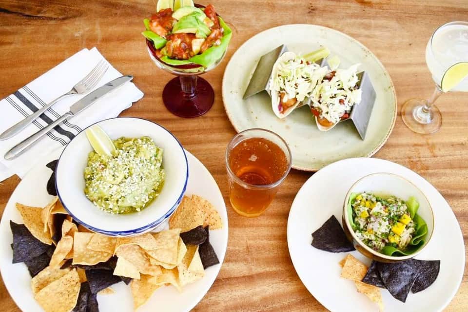 Overhead view of Mexican food platters with guacamole, tacos, and colorful drinks