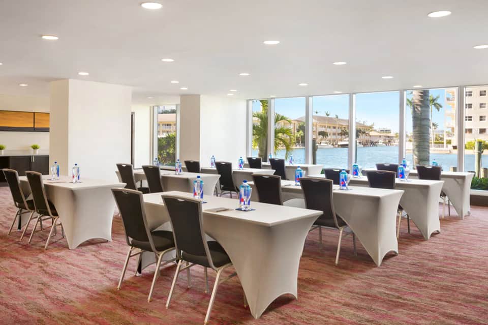 Modern conference room with white tables, black chairs, and waterfront views through expansive windows