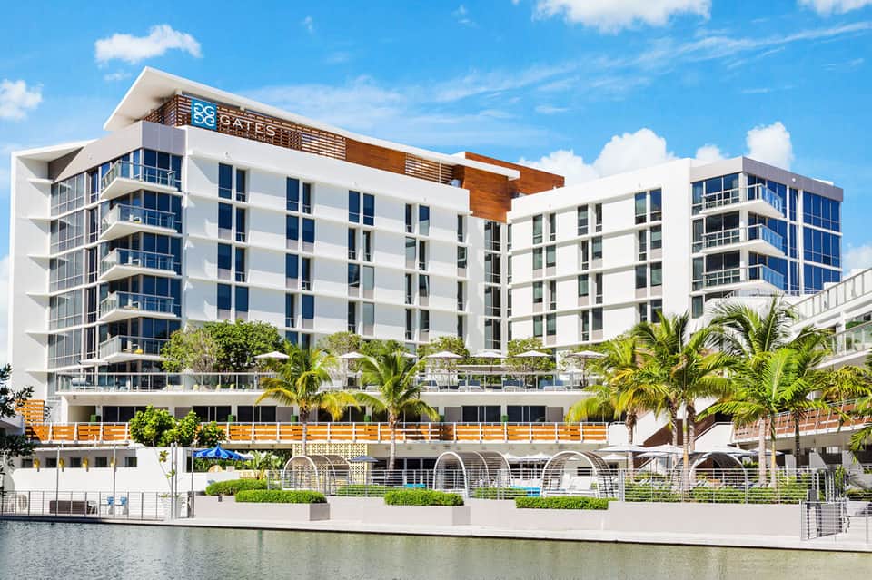 Modern waterfront hotel building with white facade, blue accents, palm trees, contemporary architecture