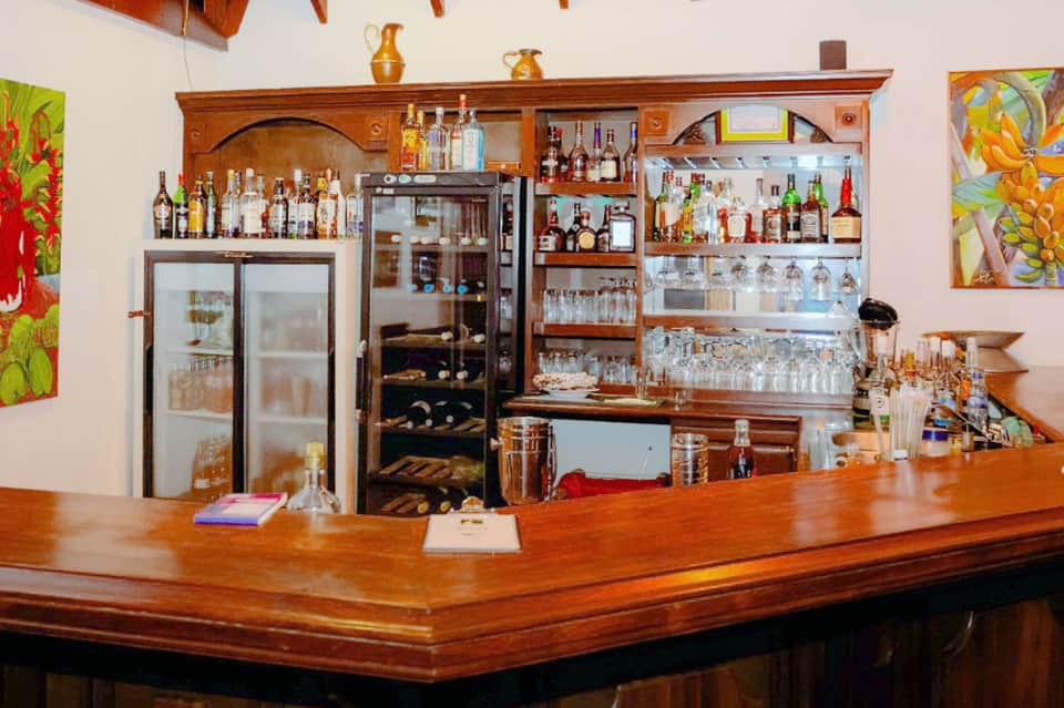 Wooden bar counter with extensive shelving displaying bottles of spirits and glassware