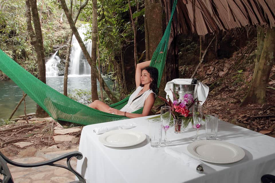 Woman relaxing in green hammock with waterfall view and elegant dining setup