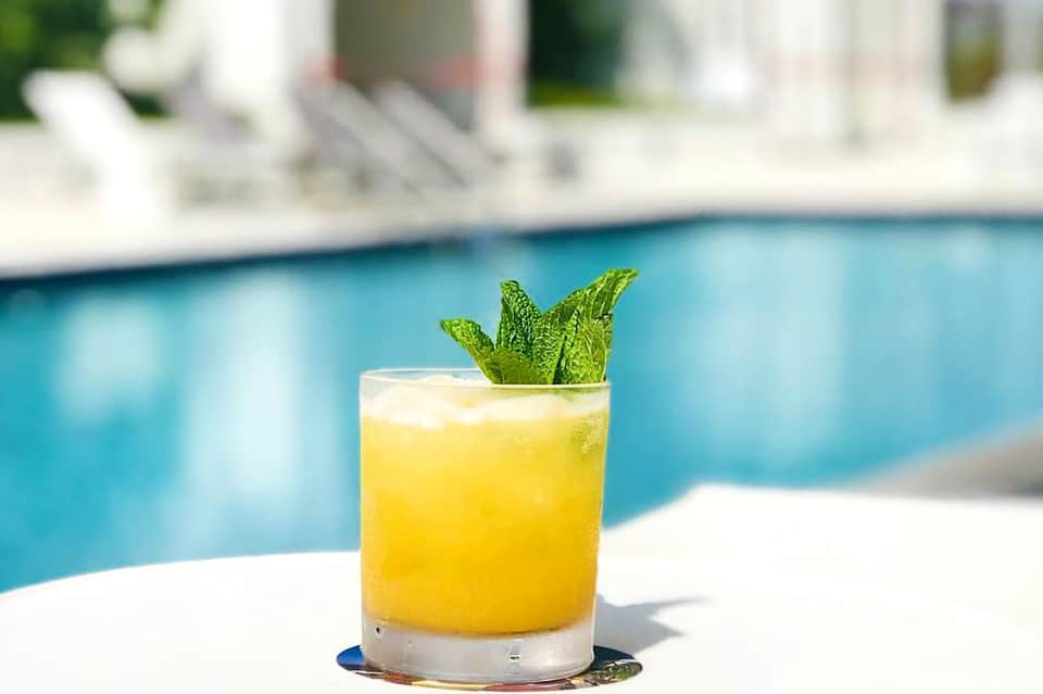 Bright yellow cocktail with mint garnish beside a swimming pool on a sunny day