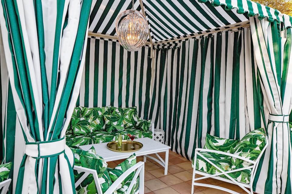 Striped green and white cabana with cushioned seating and woven light fixture