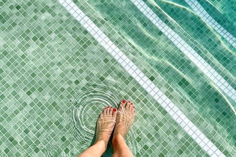 Feet dangling in green-tiled pool with rippling water and white lane divider
