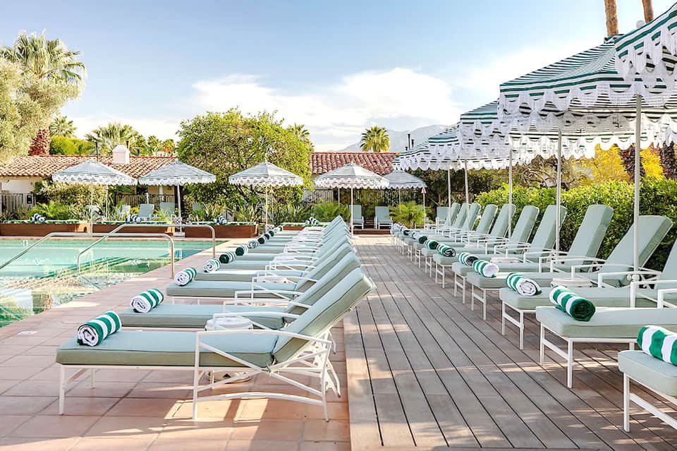 Resort pool deck with white lounge chairs, green and white striped umbrellas, pergolas, and mountain backdrop
