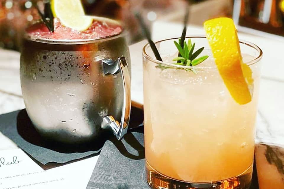 Two craft cocktails on white table: dark mojito with lime and light tropical drink with lemon twist