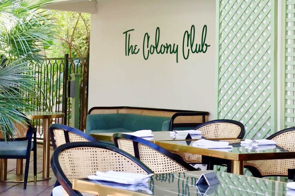 Elegant restaurant patio at The Colony Club with green lattice details, rattan chairs, and tropical foliage