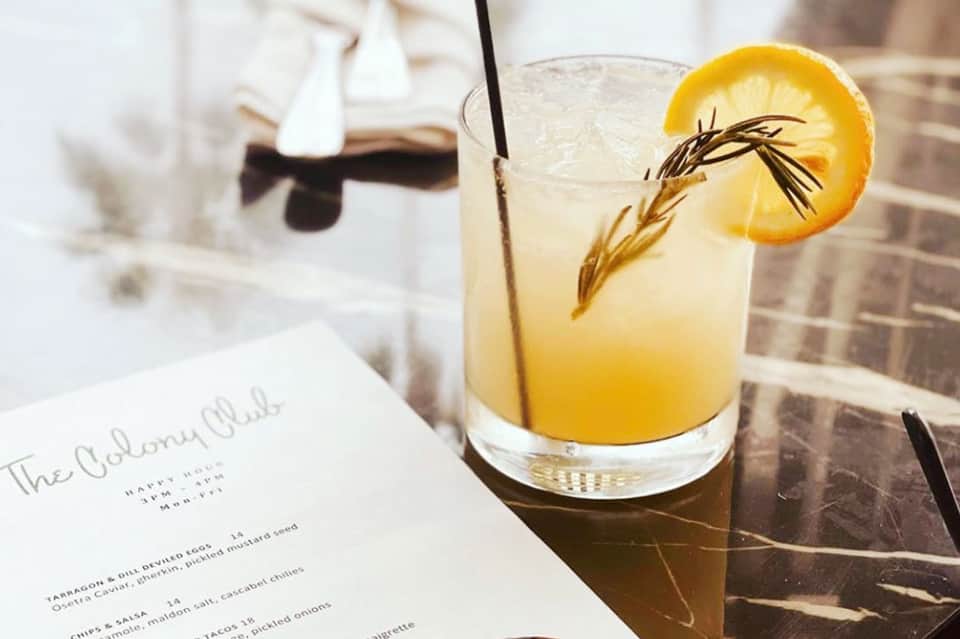 Craft cocktail with lemon slice and rosemary garnish on a table with menu at upscale restaurant