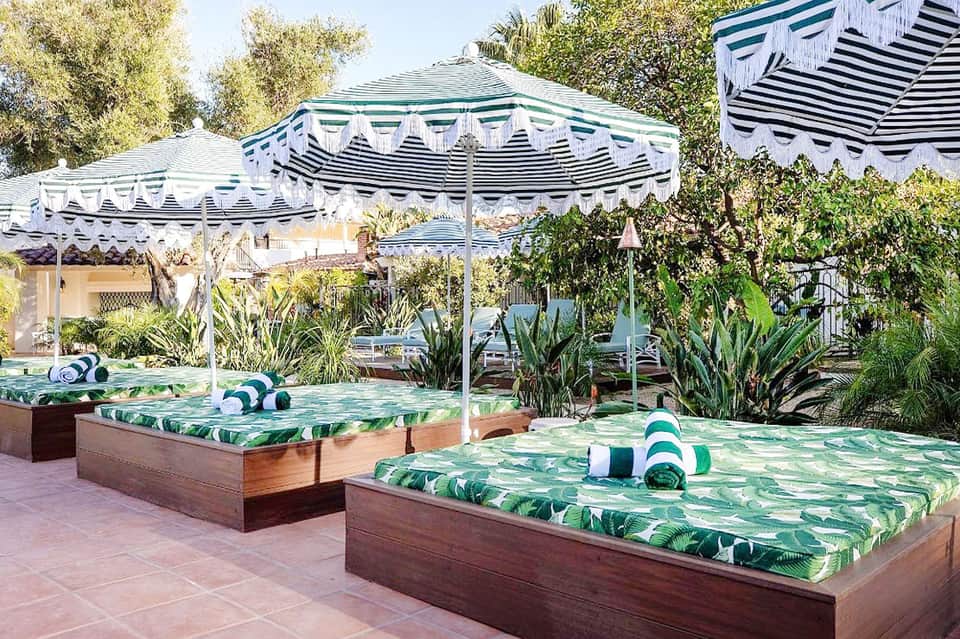 Pool loungers with tropical leaf pattern under striped umbrellas and wooden pergola