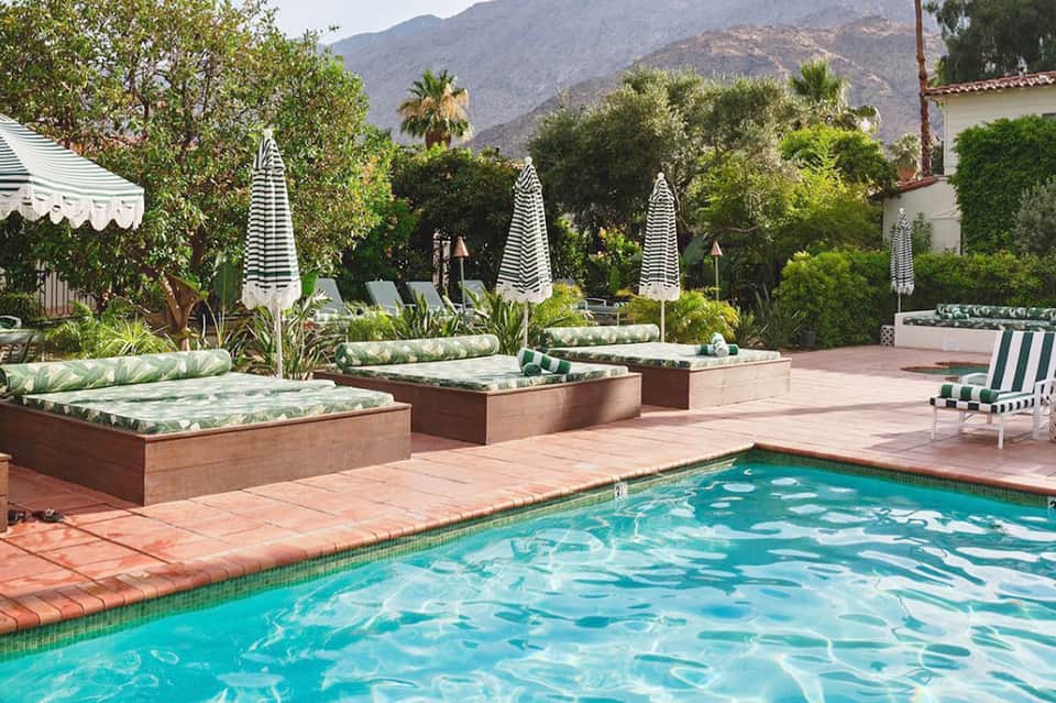 Resort pool with striped umbrellas, cushioned lounges, mountains, and lush tropical landscaping