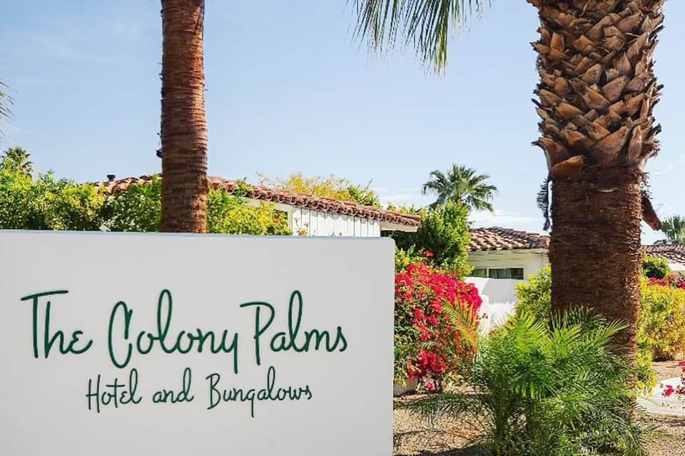 The Colony Palms Hotel and Bungalows entrance sign with palm trees and red flowers