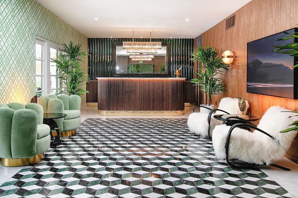 Modern hotel lobby with green patterned wallpaper, curved green chairs, wooden reception desk, and black floor