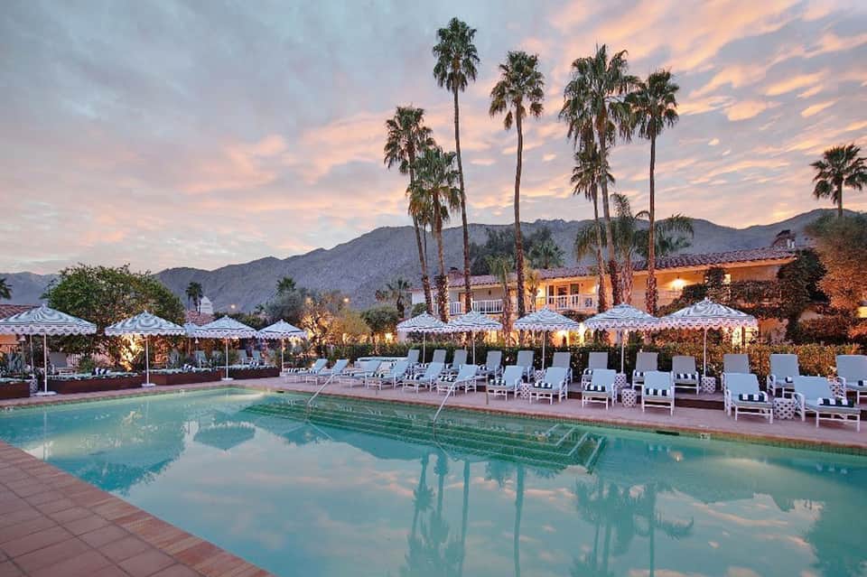 Desert resort pool at dusk with palm trees, umbrellas, and illuminated buildings