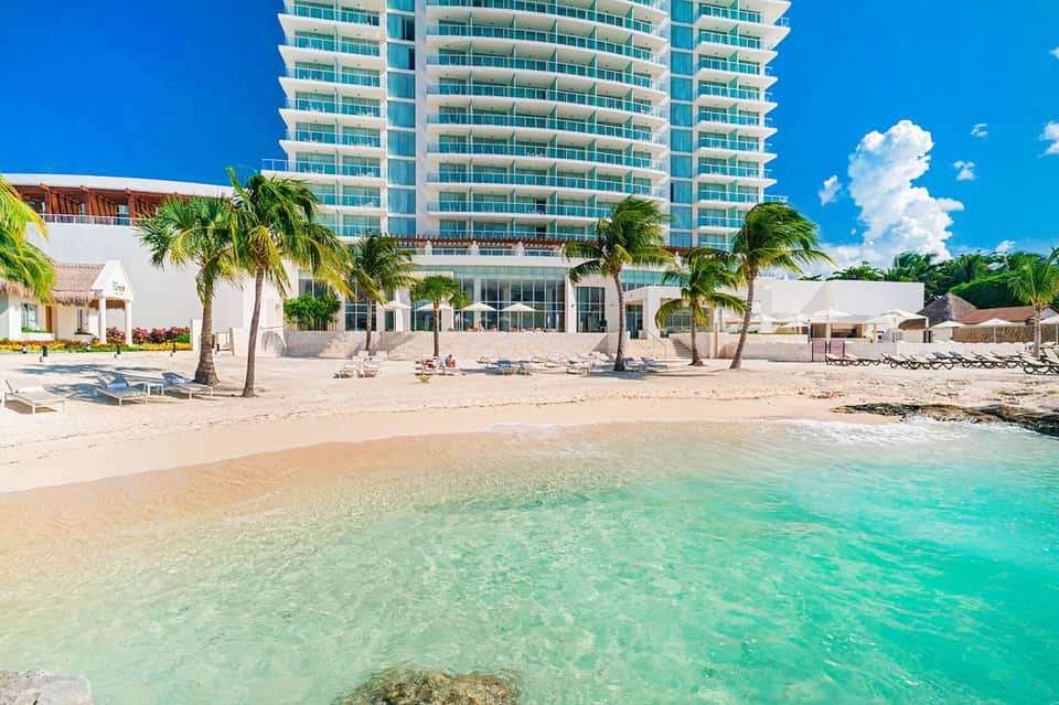 Beachfront high-rise resort with white sandy beach, turquoise shallow water, and palm trees