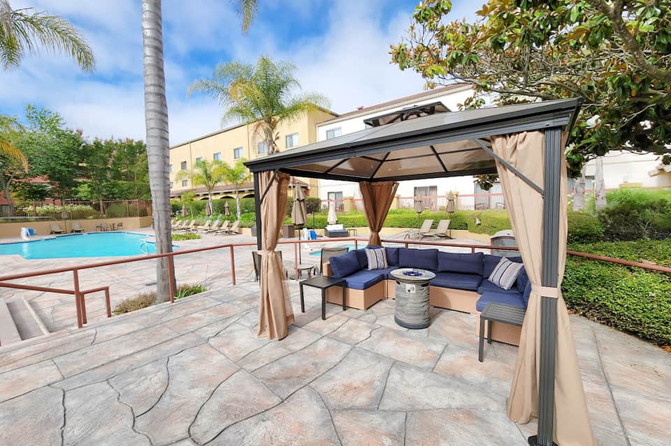 Poolside gazebo with blue cushioned seating, metal frame, and ocean view in background