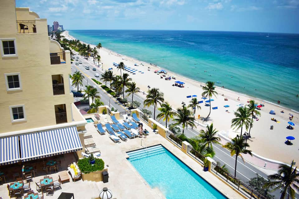 Beachfront resort with sandy beach, palm trees, swimming pool, and ocean view from aerial perspective