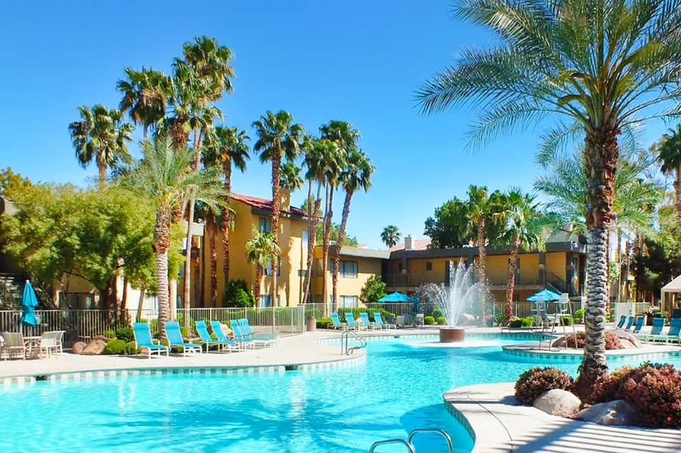 Resort pool with turquoise water, palm trees, lounge chairs, and yellow building