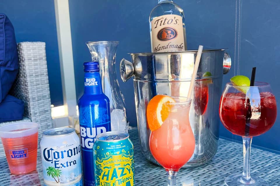 Poolside cocktail setup with beer, rum, and colorful mixed drinks in glasses with garnishes