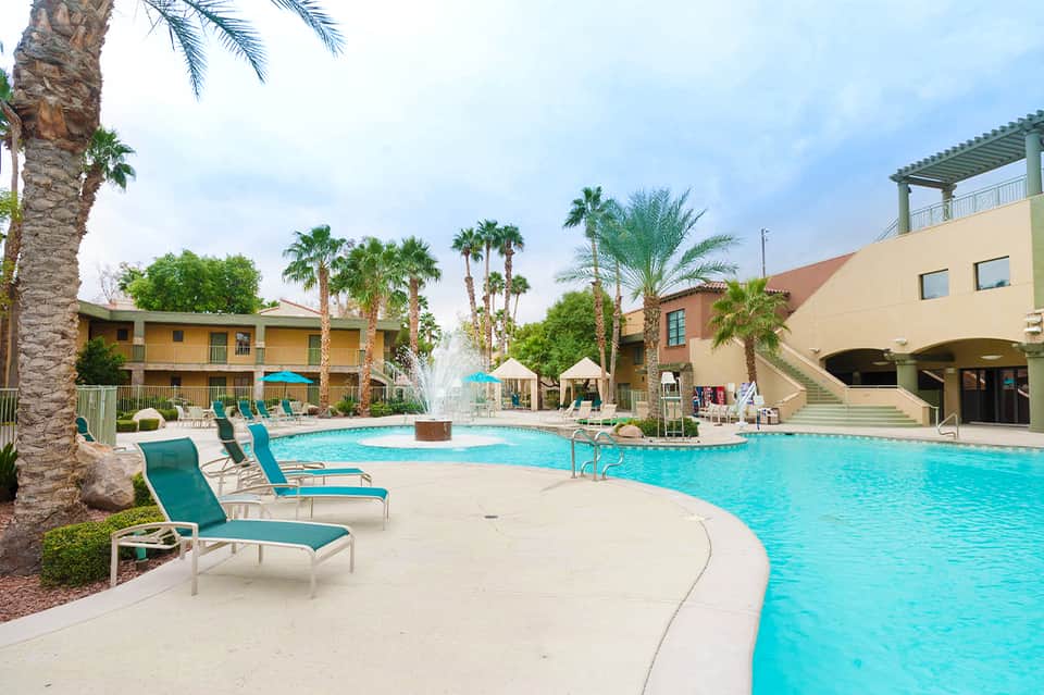 Resort courtyard with sparkling pool, palm trees, lounge chairs, and multi-story buildings
