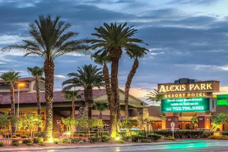 Alexis Park Resort Hotel sign at dusk with palm trees and illuminated desert landscape