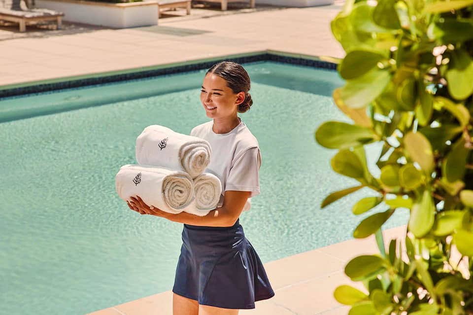 Hotel staff member holding rolled towels beside turquoise resort pool