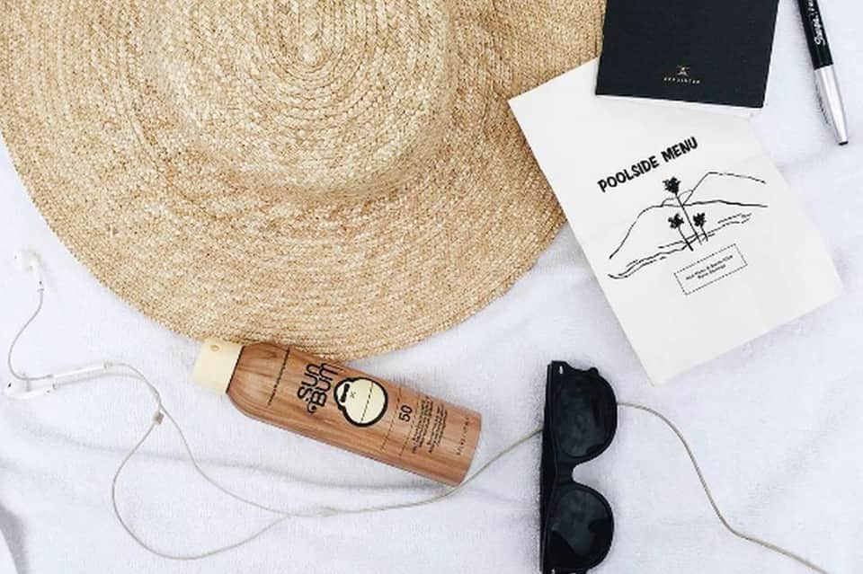 Poolside essentials: straw hat, sunscreen, sunglasses, menu, and earbuds on white towel