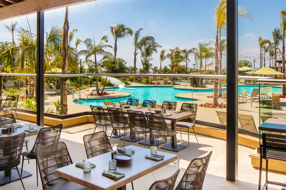 Modern resort dining area with floor-to-ceiling windows overlooking turquoise pool and palm trees