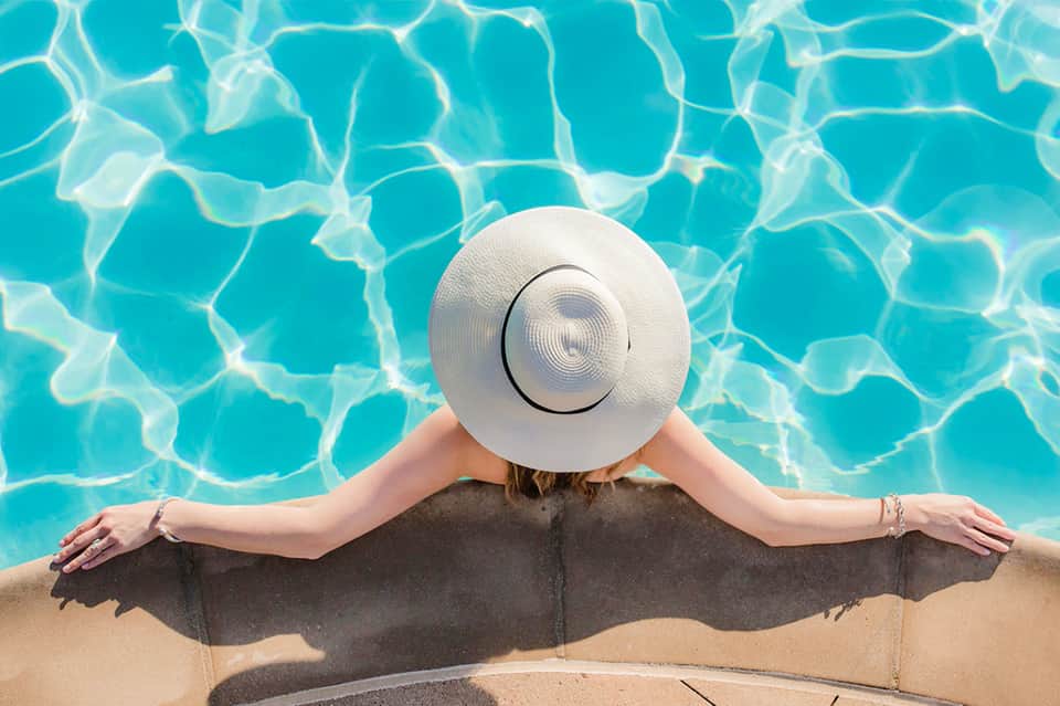 Woman in a white sun hat relaxing in a swimming pool, viewed from above