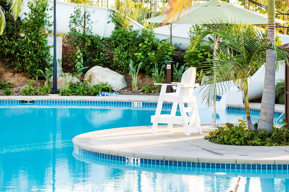 Resort pool with lifeguard stand, lush tropical landscaping, white umbrellas, and palm trees