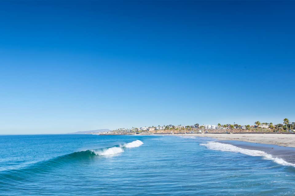 Scenic coastal beach with waves, sandy shore, and residential buildings on cliffs