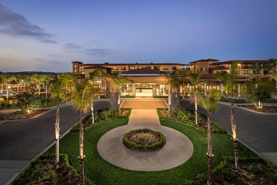 Luxury resort exterior at twilight with palm trees, lit pathways, and landscaped grounds