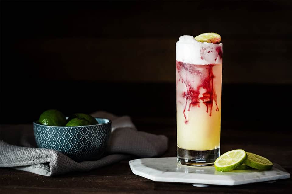 Tropical cocktail with lime garnish on marble surface with limes and linens