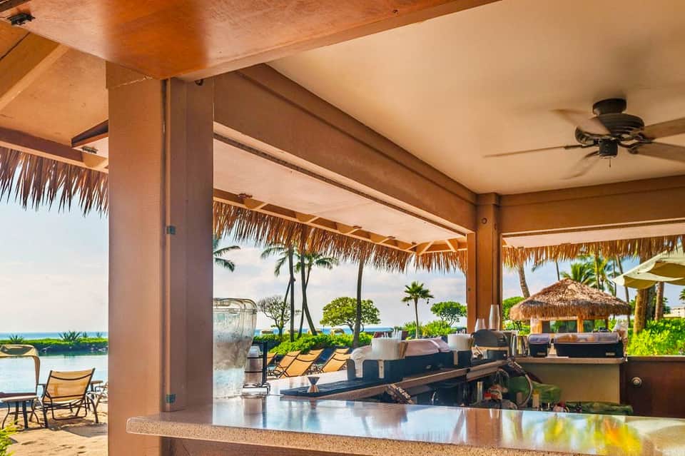 Beachfront resort bar and lounge with ocean views, thatched roof structures, and palm trees