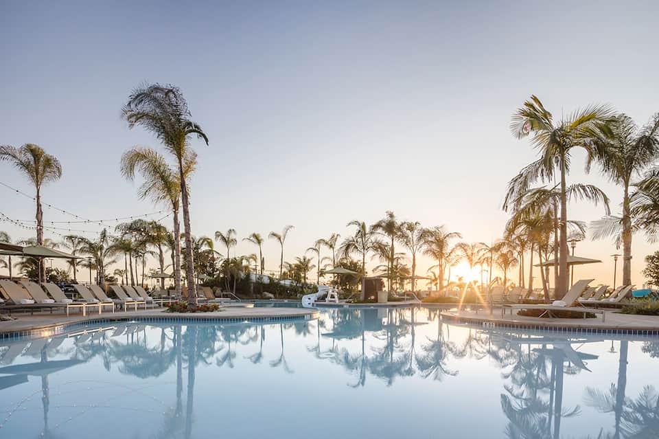 Resort swimming pool at sunset surrounded by palm trees and lounge chairs with clear reflections