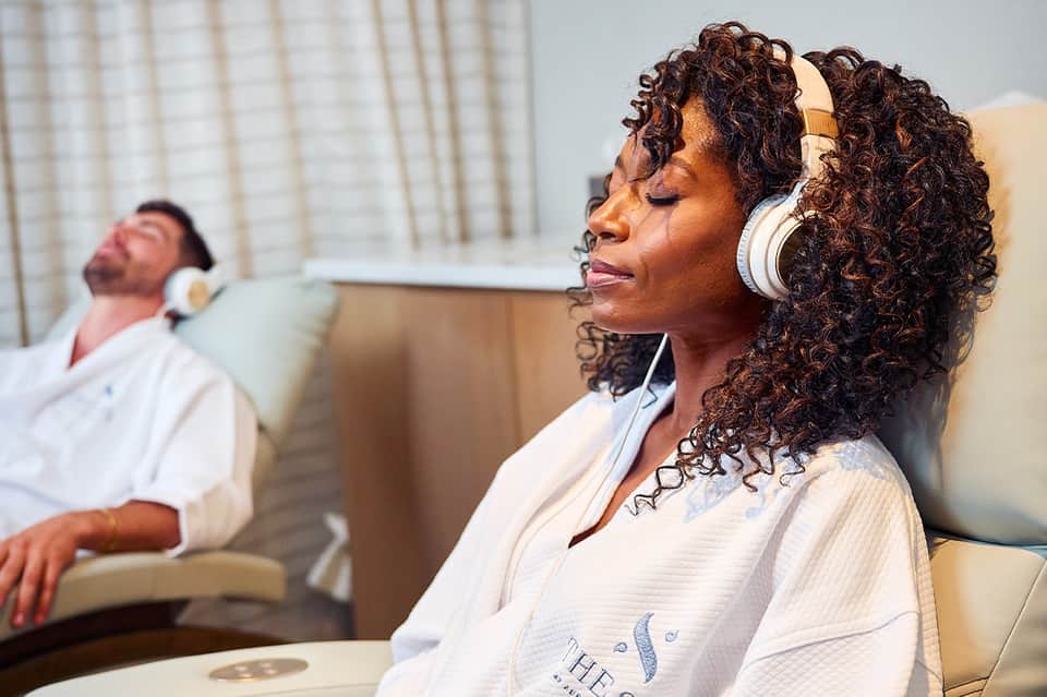 Woman wearing headphones relaxing in spa lounge chair with man in background