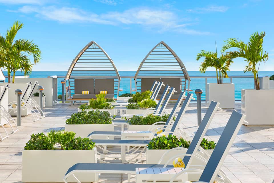 Beachfront resort patio with boat-shaped cabanas, lounge chairs, and ocean view