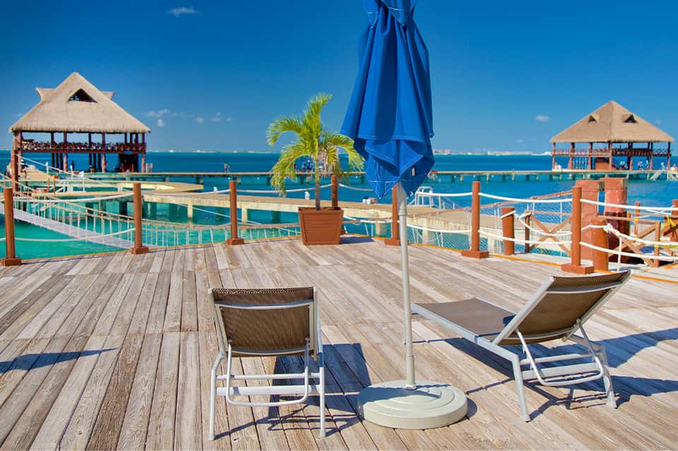 Waterfront deck with thatched cabanas, lounge chairs, and turquoise water views