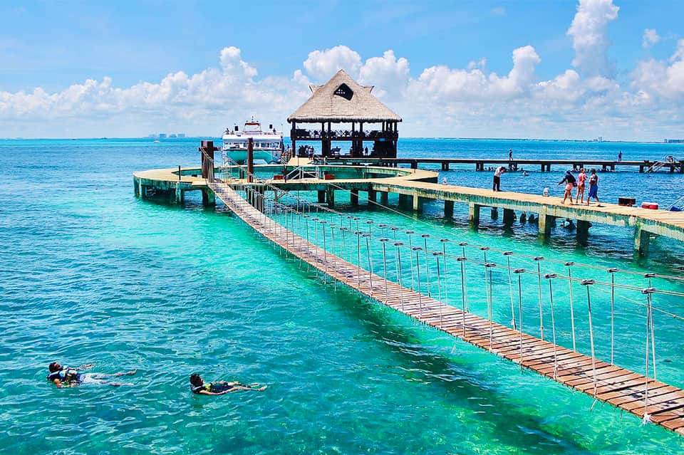 Tropical pier with wooden walkway, thatched-roof pavilion, and crystal turquoise water for snorkeling