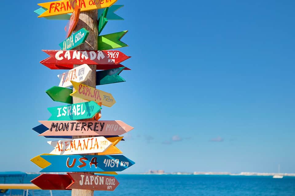 Colorful directional signpost listing international destinations with distances against blue sky