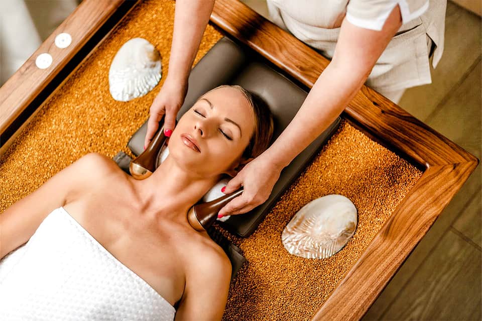 Woman receiving spa massage treatment on wooden table with seashell decorations and natural products