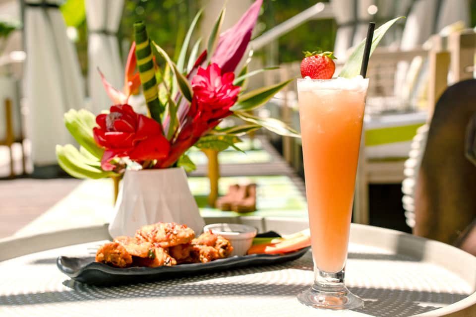 Tropical cocktail with appetizers on a table with red flowers and resort backdrop