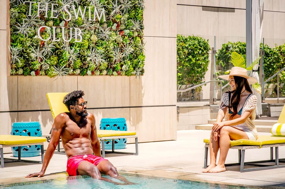 Resort pool area with guests, living plant wall, yellow loungers, and modern architecture