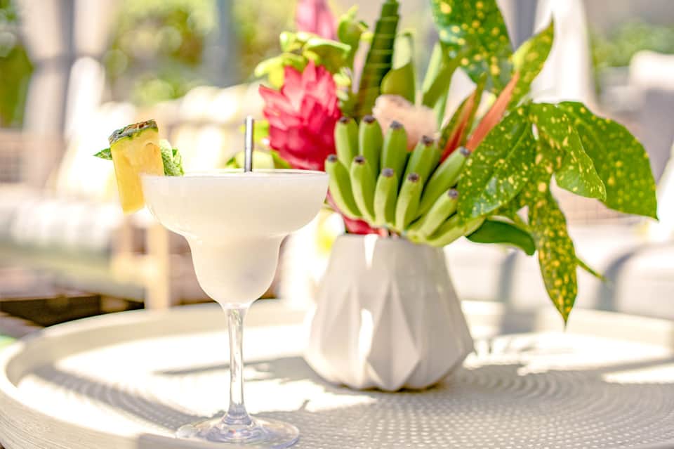 Tropical cocktail with pineapple garnish and pink flower arrangement on table