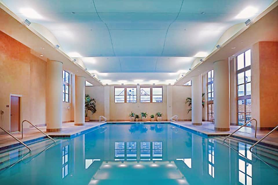 Indoor lap pool with light blue ceiling, columns, and large windows in contemporary setting