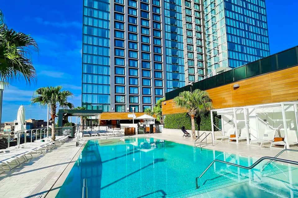 Modern high-rise hotel with rooftop pool deck featuring turquoise water and palm trees