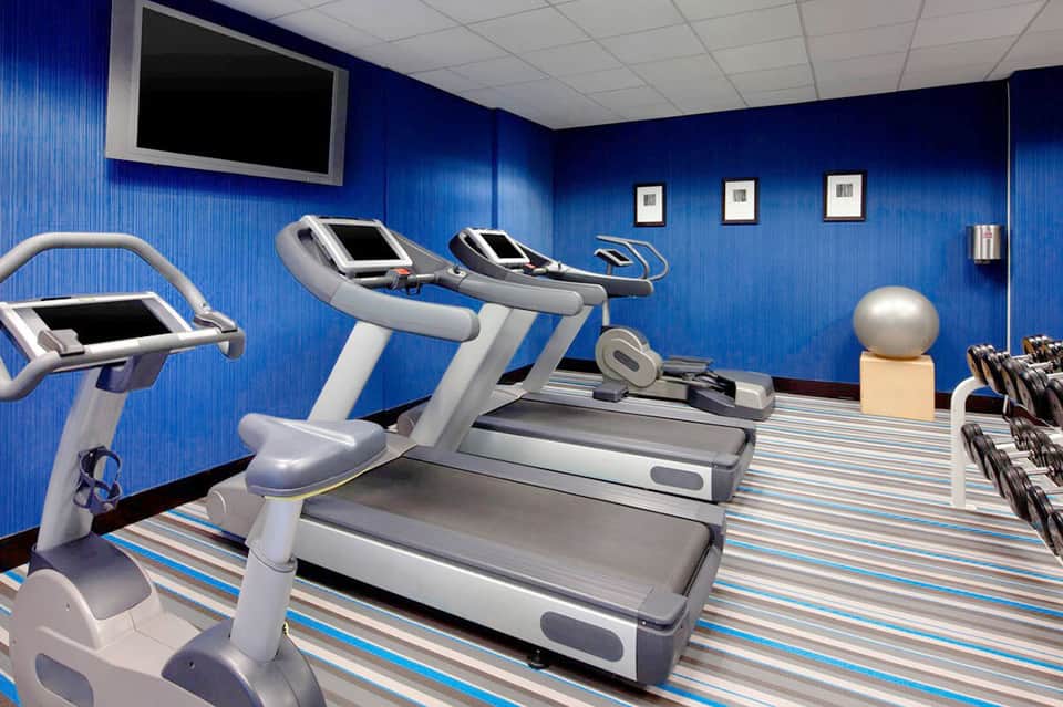 Modern fitness center with blue walls, treadmills, stationary bikes, exercise equipment and flat-screen monitor