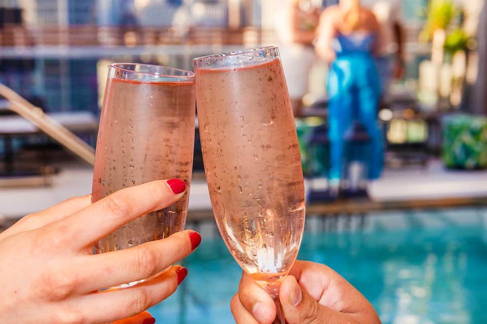 Two champagne glasses toasting by a resort pool with blurred guests in background